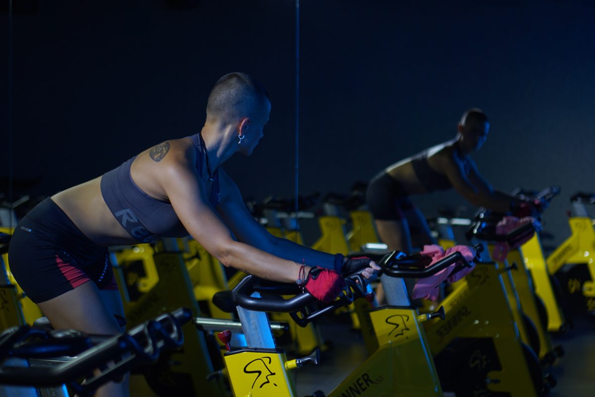 Rider alone on a spin bike in a dark studio, rows of empty bikes around her
