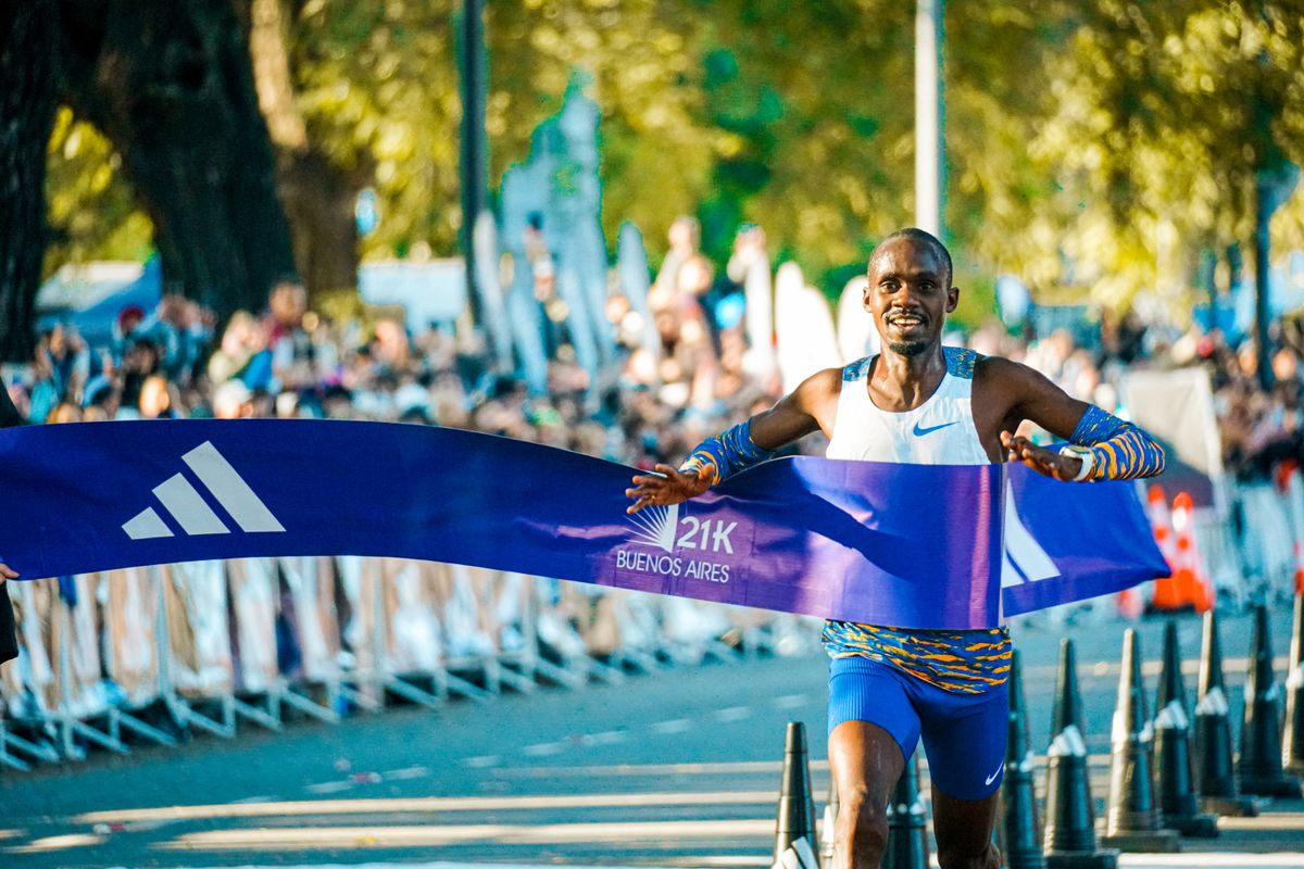 Runner breaking the finish tape with arms spread wide in front of a crowd
