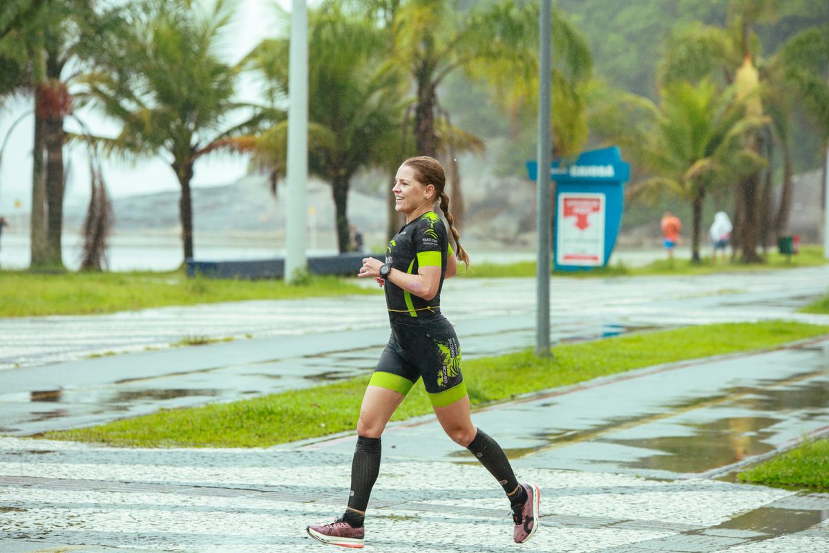 Female athlete in race kit running strongly along a palm-lined seafront path