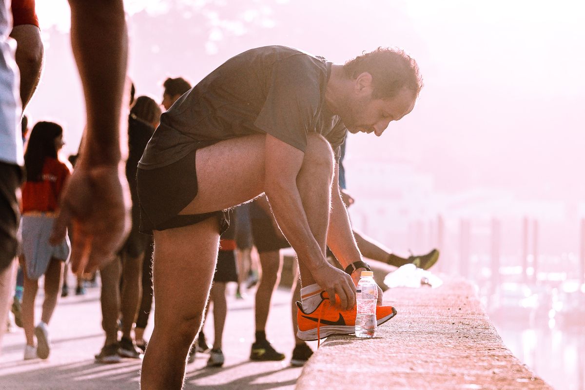 Runner tying a shoelace on a waterfront wall at sunrise, focused before setting off