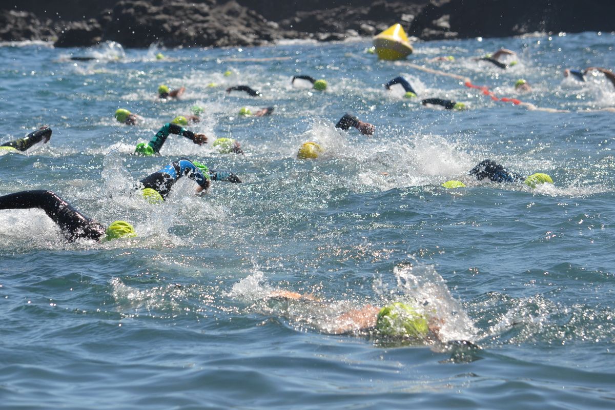 Pack of wetsuited open water swimmers in bright caps passing a yellow marker buoy