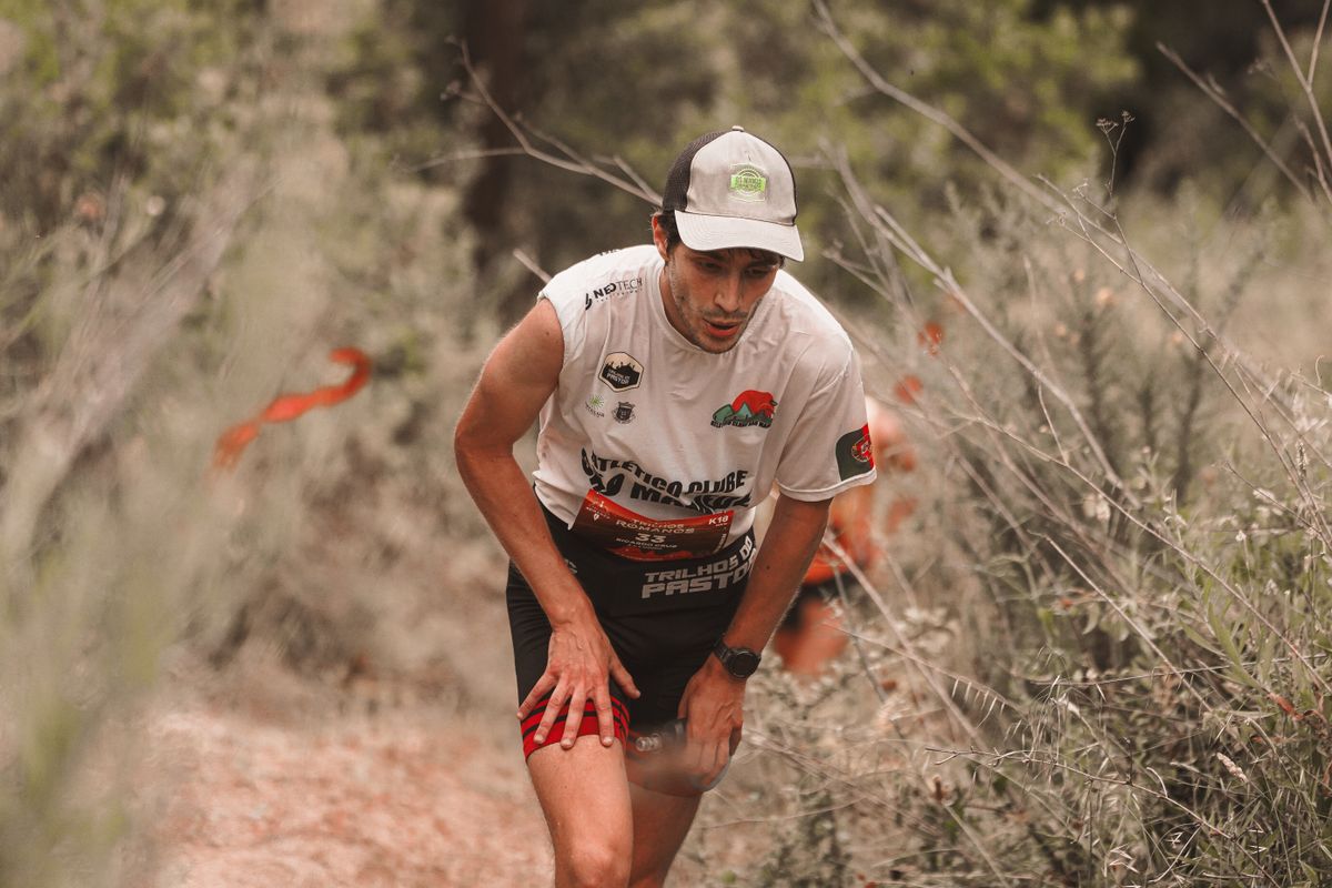 Trail runner pushing up a climb with hands on thighs, working through a hard effort