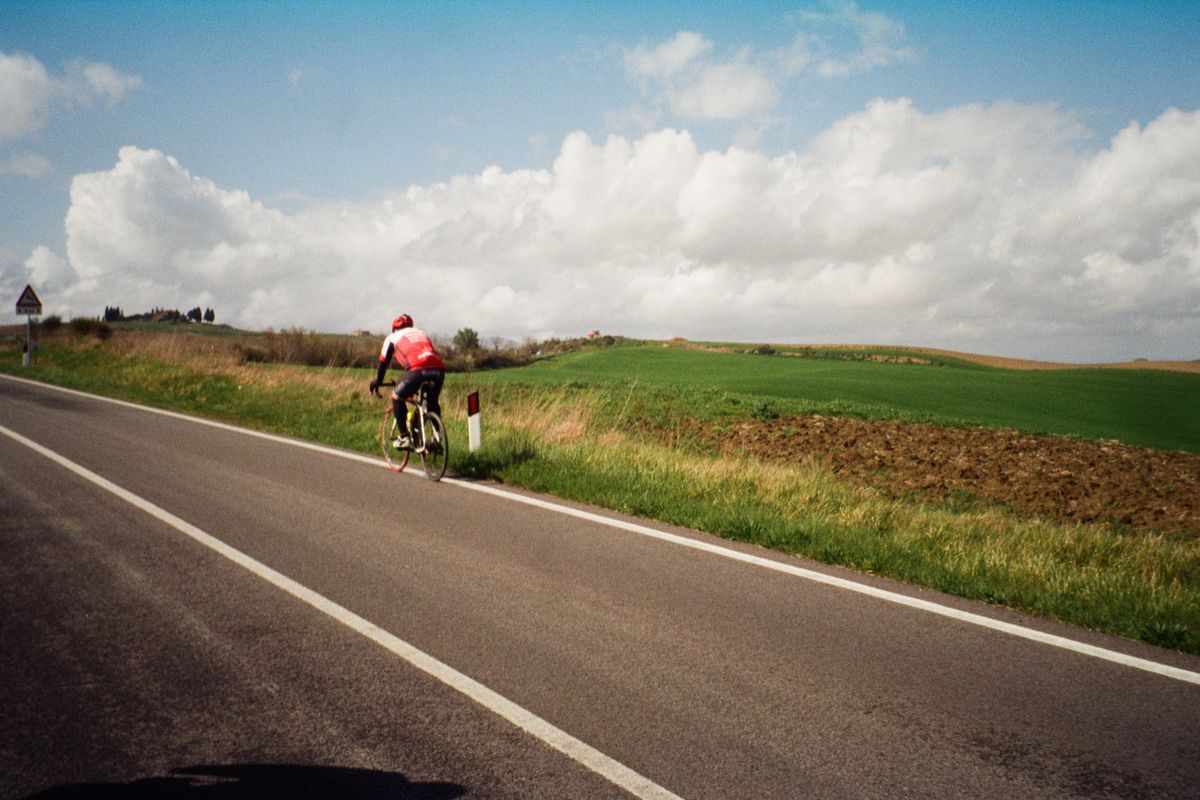 Cyclist riding alone along an empty country road past green fields